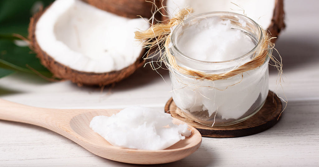 Still life of two coconuts, one of them cut in half, with a jar of coconut oil and a wooden spoon